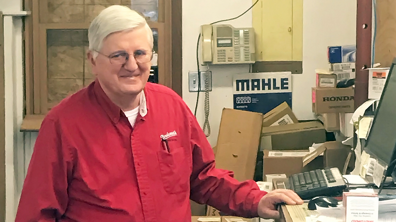 Man with white hair and wearing red button down shirt standing at a counter