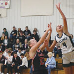 three female basketball players with two in black uniforms and one in white that is jumping